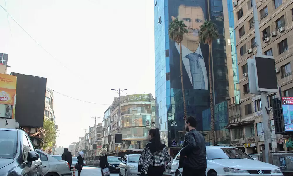 People walk near a poster depicting Syria’s President Bashar al-Assad in Damascus, after last week’s rebel seizure of Aleppo marked the biggest offensive for years, Syria December. Photo: Reuters