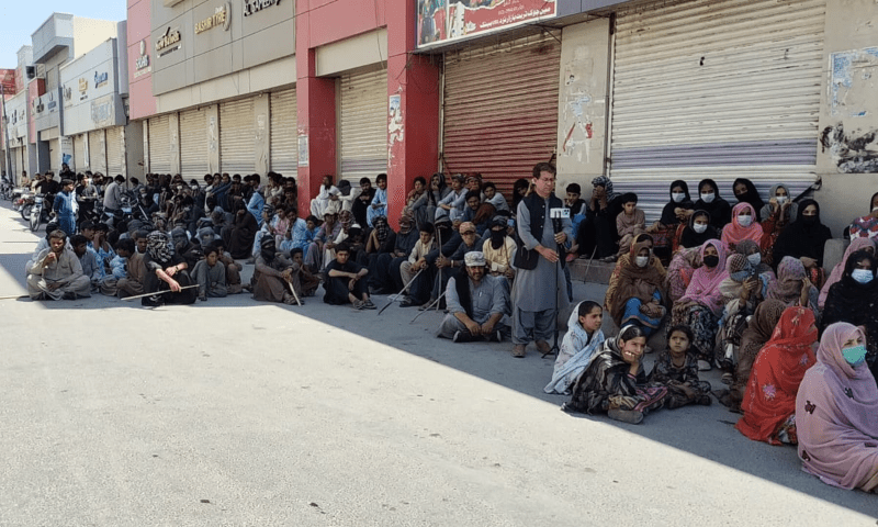 Protesters sit on the road as shops are closed in the background in Gwadar on March 22. — Asad Baloch