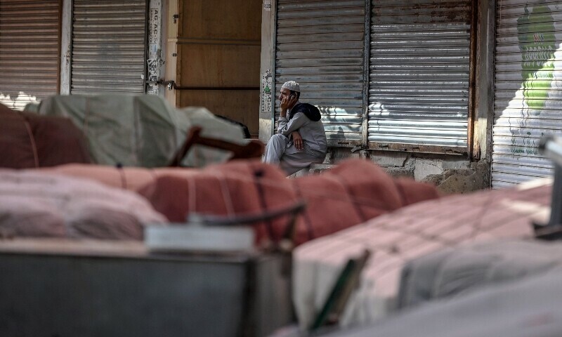 A labourer speaking on his mobile phone sits outside the closed shops to show their solidarity with Palestinians, in Karachi on April 26, 2025, amid the ongoing Gaza conflict. — AFP