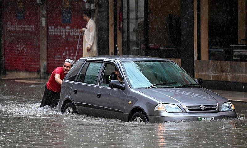  A man pushes a car through a flooded street during heavy monsoon rains in Rawalpindi on July 17.  — AFP 