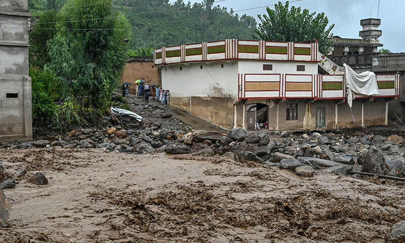 Villagers (center, L) stand near a building as floodwater levels rise in Khyber Pakhtunkhwa’s Buner district on August 18. — AFP