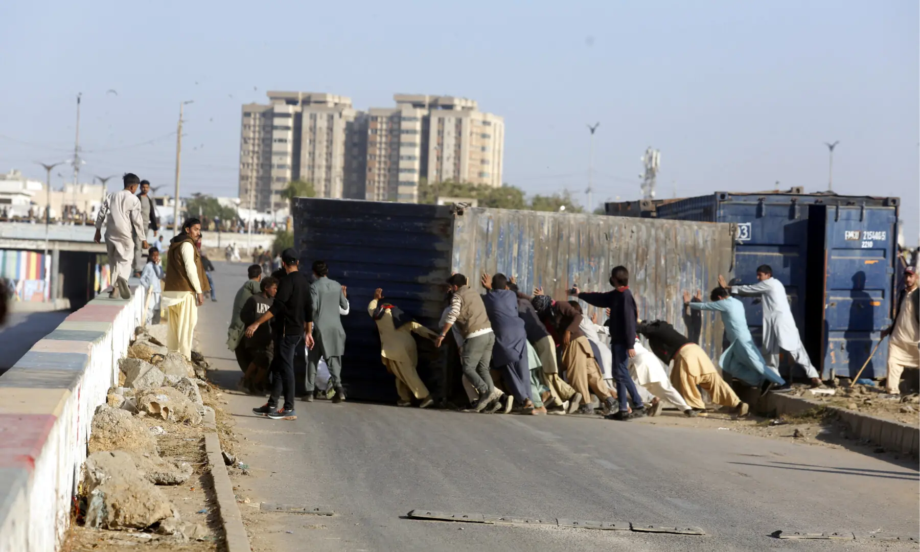 People push aside containers that had been placed to block a route in Karachi. &mdash; Shakil Adil/ White Star