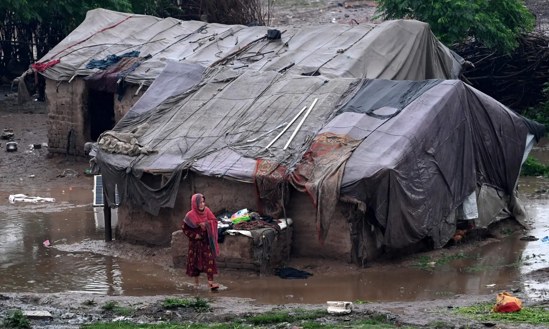 A girl walks through a pool of water near makeshift shelters after heavy rainfall in Peshawar on April 3, 2026. &mdash; AFP